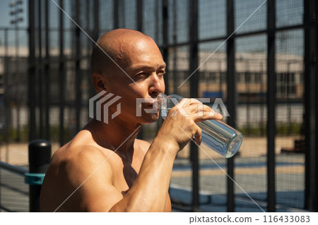 Athletes handsome man drinking water on outdoor sports ground. Water balance for heat season for active workout. Close up. Athletes handsome man drinking water on outdoor sports ground. Water balance for heat season for active workout. Close up. 116433083