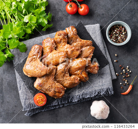 Roasted chicken wings bbq with tomato and fresh herb on a black slate on a dark background Roasted chicken wings bbq with tomato and fresh herb on a black slate on a dark background 116433264