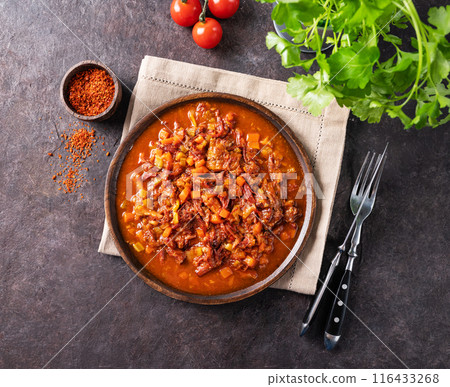 Stewed oxtails with vegetables in a wooden plate on a dark background with fresh tomatoes and herbs. Stewed oxtails with vegetables in a wooden plate on a dark background with fresh tomatoes and herbs. 116433268
