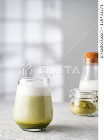 Green matcha latte in a glass on a gray background with morning shadows from the window Green matcha latte in a glass on a gray background with morning shadows from the window 116433271