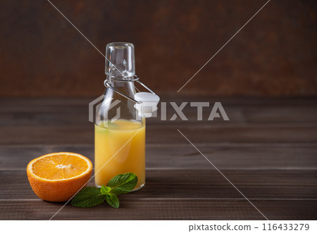 Fresh orange juice in bottle with citrus fruit and mint on a brown wooden background. Fresh orange juice in bottle with citrus fruit and mint on a brown wooden background. 116433279