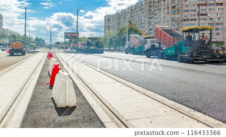 Asphalt paver, roller and truck on the road repair site during asphalting timelapse. Road construction equipment. 116433366