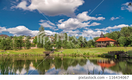 View of the pond, blooming meadow, forest and cottages in village at summer timelapse hyperlapse 116434067