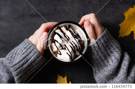 hands holding a cup of hot chocolate with marshmallow on a dark gray background. hands holding a cup of hot chocolate with marshmallow on a dark gray background. 116434773