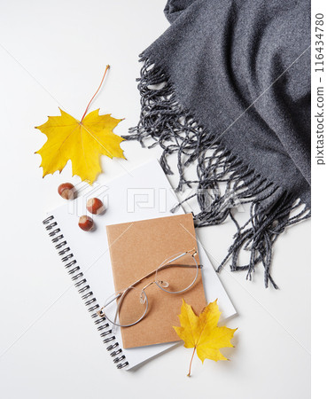 Concept cozy autumn flat lay with yellow maple leaves on notepad with eyeglasses and gray scarf  116434780