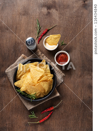 Corn chips nachos with salsa and cream sauce, herbs, salt and chili pepper on a wooden background. 116434840