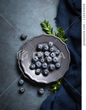 Juicy and ripe blueberries on a gray plate on a dark blue background with a napkin. Juicy and ripe blueberries on a gray plate on a dark blue background with a napkin. 116434856
