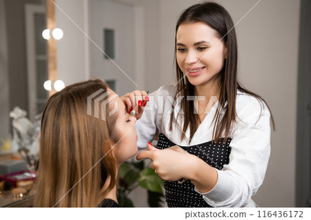 Makeup artist applies base color across client eyelid. Specialist sets foundation for multi-dimensional effect during makeup process 116436172