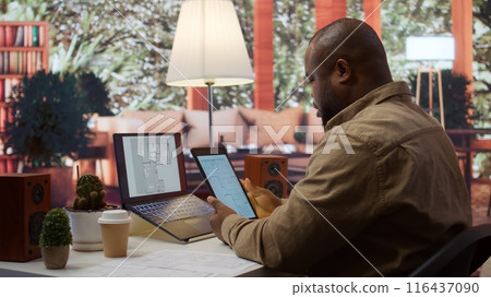 Businessman searching for commercial office spaces from his home workstation, doing a blueprints review and drafting building layouts to find the perfect startup property. Real estate. Camera B. Businessman searching for commercial office spaces from his home workstation, doing a blueprints review and drafting building layouts to find the perfect startup property. Real estate. Camera B. 116437090