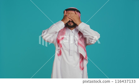 Person doing three wise monkeys sign in studio, wears muslim religious attire and headdress. Young adult covering his eyes, mouth and ears to show important metaphor concept. 116437133