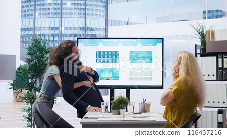 Employee choking in office, being helped by quick thinking coworker performing Heimlich maneuver. Worker offering first aid to colleague while coworker calls for ambulance, camera B Employee choking in office, being helped by quick thinking coworker performing Heimlich maneuver. Worker offering first aid to colleague while coworker calls for ambulance, camera B 116437216