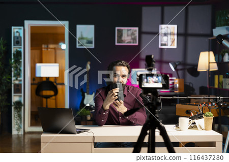 Tech expert paid by sponsor to endorse portable V mount battery, filming with professional camera in studio. Man contracted by company to advertise lithium li-ion charging device to audience Tech expert paid by sponsor to endorse portable V mount battery, filming with professional camera in studio. Man contracted by company to advertise lithium li-ion charging device to audience 116437280