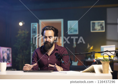 Man in studio endorsing laptop from brand sponsoring video, talking in professional microphone. Content creator does influencer marketing by promoting notebook, recording with high tech mic Man in studio endorsing laptop from brand sponsoring video, talking in professional microphone. Content creator does influencer marketing by promoting notebook, recording with high tech mic 116437296