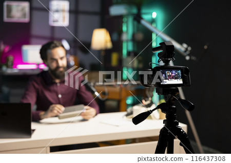 Focus on tech guru in blurry background doing technology review of wireless portable speaker. Close up shot of professional camera used by influencer to record music playing device review 116437308