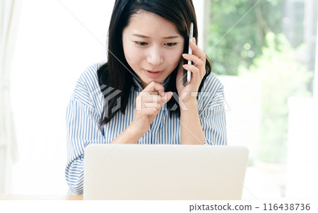 一位年輕的女士在看電腦的同時打電話 116438736