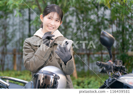 A woman riding a motorcycle and looking at her smartphone 116439581