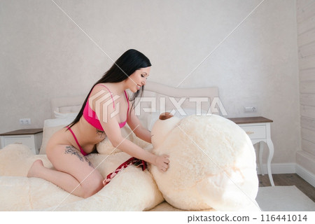 Woman In Pink Lingerie Plays With Large White Teddy Bear On Bed 116441014