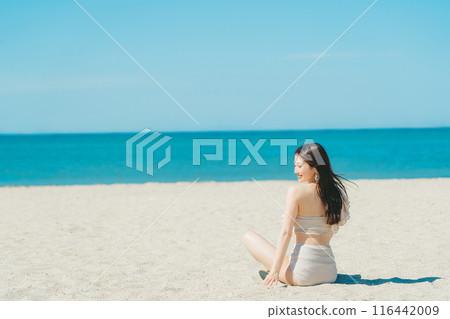 Young woman in swimsuit sitting on sandy beach 116442009