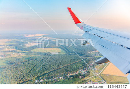 View of airplane wing, blue skies and green land during landing. Airplane window view. 116443557