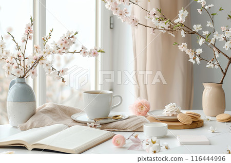 Table with a white cup, a plate of cookies, and a vase of flowers near windows 116444996