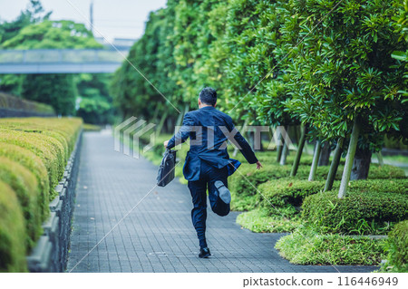 A middle-aged businessman in a suit running through the city 116446949