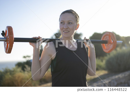 A woman is lifting a weight bar with a smile on her face 116448522