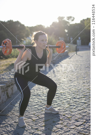 A woman is lifting a weight in a park A woman is lifting a weight in a park 116448534