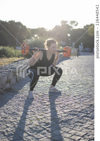 A woman is lifting a weight in a park 116448541