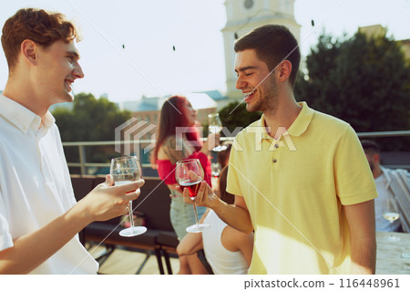 Friends gather for sunny celebration, raising their glasses in toast to happiness of moment. Outdoor party. Friends gather for sunny celebration, raising their glasses in toast to happiness of moment. Outdoor party. 116448961