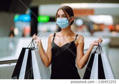 Fashionable woman in protective medical mask with shopping bags walking in the mall. Covid-19. 116451255