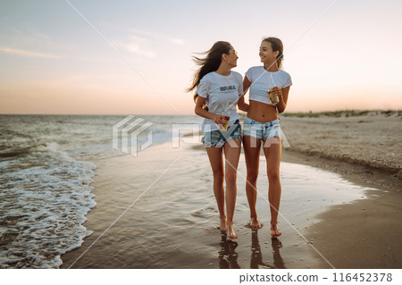 Beautiful two girls with glasses is holding a bottle with beer in her hands at the beach.. Summer lifestyle. Beautiful two girls with glasses is holding a bottle with beer in her hands at the beach.. Summer lifestyle. 116452378