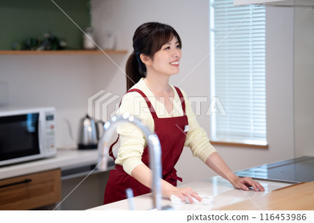A middle-aged woman in an apron wiping down the kitchen A middle-aged woman in an apron wiping down the kitchen 116453986