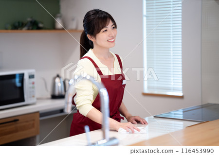A middle-aged woman in an apron wiping down the kitchen 116453990