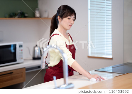 A middle-aged woman in an apron wiping down the kitchen A middle-aged woman in an apron wiping down the kitchen 116453992