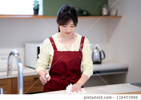 A middle-aged woman in an apron wiping down the kitchen 116453998