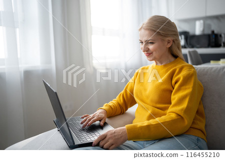 A blonde woman is working with intense focus from her home office, typing on a laptop 116455210