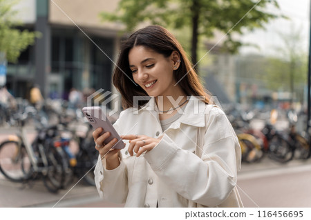 A modern commuter, this young woman pauses to check her itinerary, embodying the rhythm of city life while waiting at the bus station A modern commuter, this young woman pauses to check her itinerary, embodying the rhythm of city life while waiting at the bus station 116456695