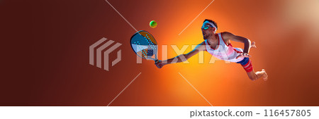 Competitive man playing beach tennis, in motion hitting ball with racket against orange studio background in neon light Competitive man playing beach tennis, in motion hitting ball with racket against orange studio background in neon light 116457805