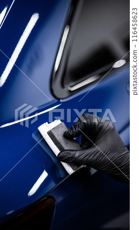 Image shows a person applying a ceramic coating to the surface of a blue car 116458623