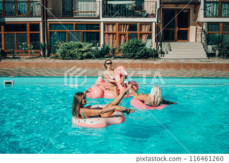 A group of people are in a pool with pink and white floats. Scene is fun and lighthearted. 116461260