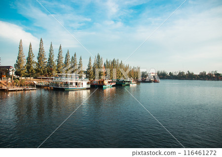 A serene river scene with boats docked by a pier and trees lining the shore under a partly cloudy sky in Kampot, Cambodia A serene river scene with boats docked by a pier and trees lining the shore under a partly cloudy sky in Kampot, Cambodia 116461272