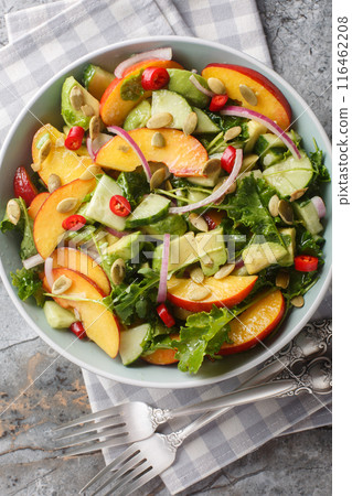Peach avocado salad with onion, chili, arugula, spinach and pumpkin seeds close-up in a bowl. Vertical top view 116462208