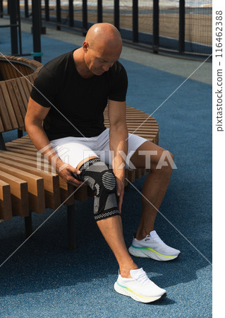 Man putting knee brace to support painful leg. Athlete bodybuilder leg wearing knee support brace or elastic kneecap bandage. Sleeve for compression. Health problems and pain. 116462388