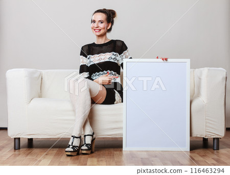 woman on sofa holding blank presentation board. 116463294