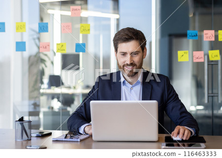 Successful smiling man working with laptop inside office, satisfied with results businessman typing on keyboard, mature boss in business suit at workplace. 116463333