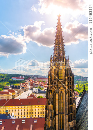 St. Vitus Cathedral ornate side spire towers over the surrounding landscape with city and greenery in the backdrop under a partly cloudy sky. 116463334