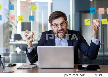 Angry boss inside office at workplace, experienced businessman looking at camera shouting, senior mature man in business suit working with laptop. 116463953
