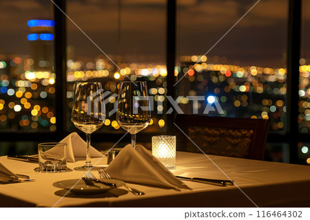 Elegant dining setup with glasses, candlelight and a cityscape at dusk Elegant dining setup with glasses, candlelight and a cityscape at dusk 116464302
