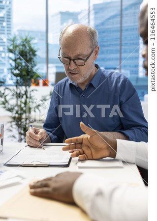 Senior client agreeing to retirement plan option terms with financial planner, signing the contract to secure life savings for the future. Old couple receive professional advice from expert. 116464553