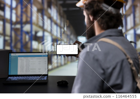 Storage room engineer using smartphone with white display, reading cargo details on distribution contracts. Supervisor with helmet looking at phone with blank mockup layout, warehouse logistics. 116464555